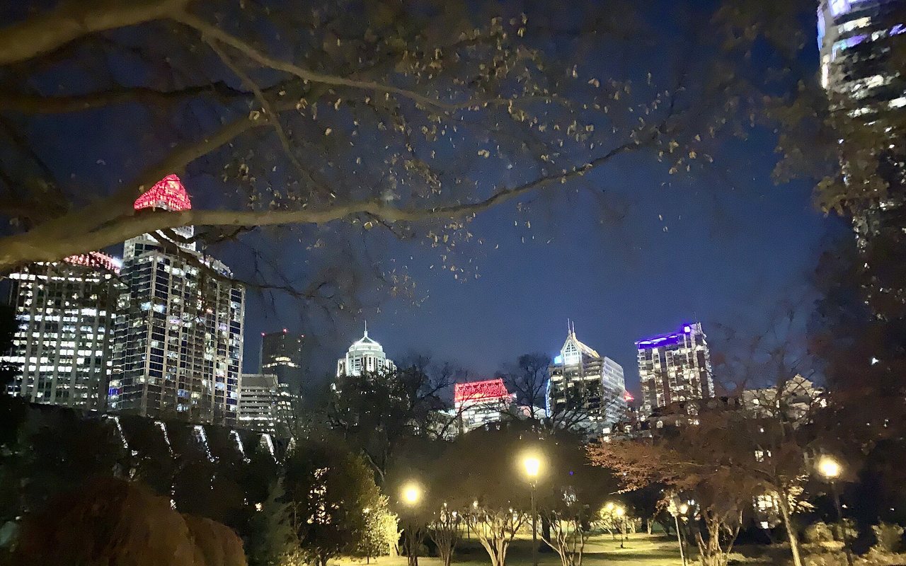 Fourth Ward Park in Charlotte at dusk: lit footpaths under bare trees, with the uptown towers behind.
